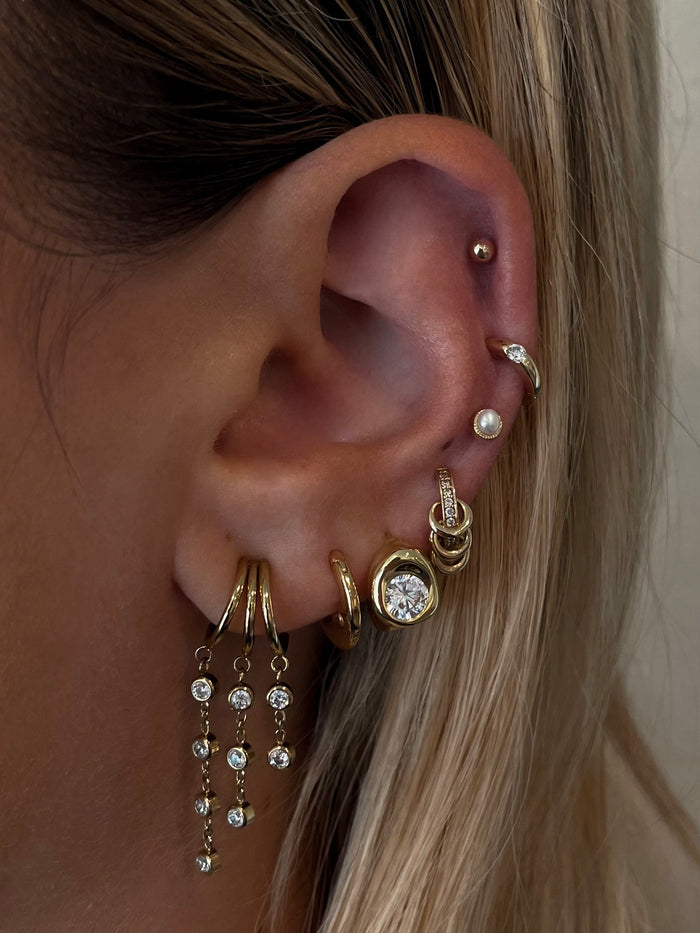 Close-up of an ear with multiple gold and crystal earrings against a neutral background