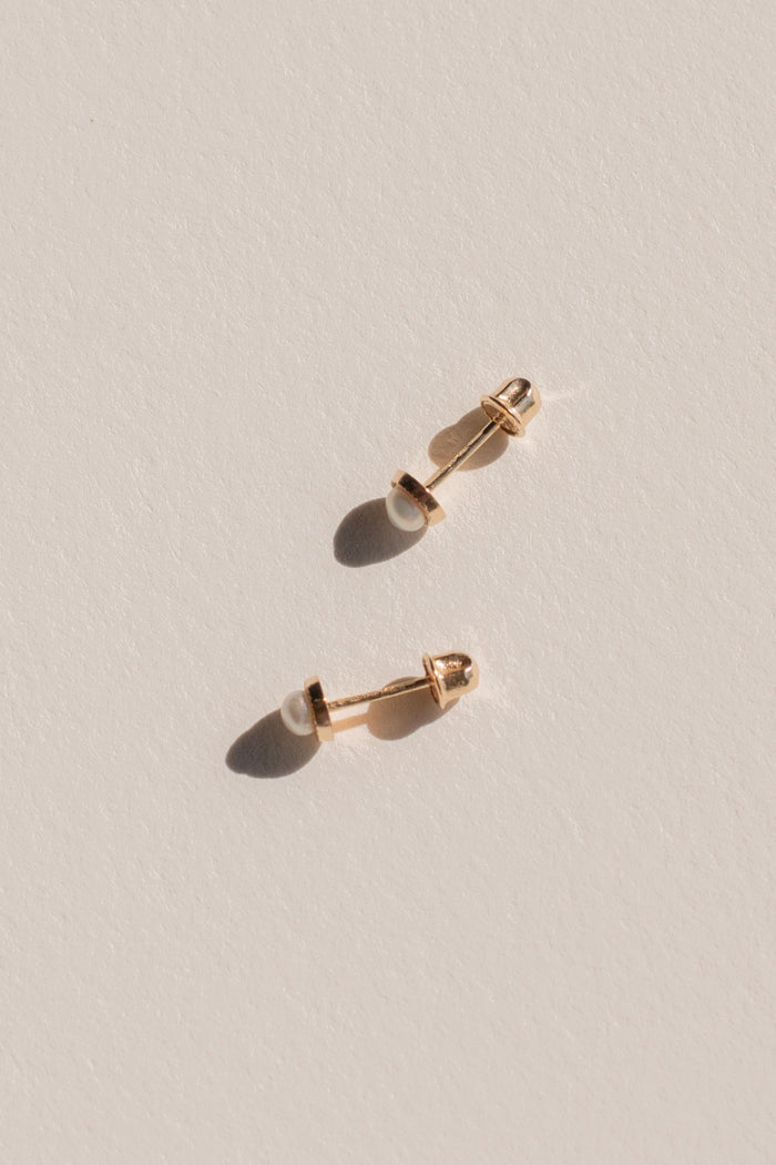 Close up of gold and pearl earrings on a neutral background