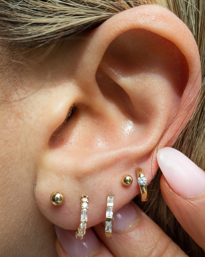 Close-up of an ear with multiple gold and crystal earrings