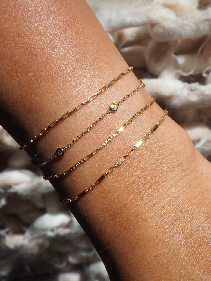 A wrist with dainty gold chain bracelets on a neutral background