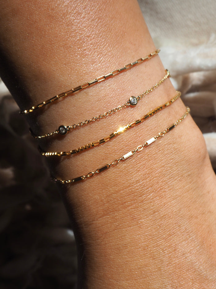 A wrist with dainty gold chain bracelets on a neutral background