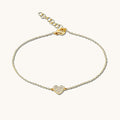 Close up of a gold chain bracelet with a diamond-encrusted heart charm on a white background