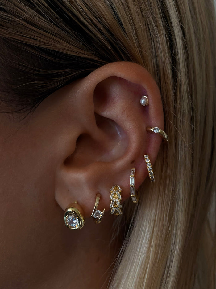 Close-up of an ear with multiple gold and crystal earrings