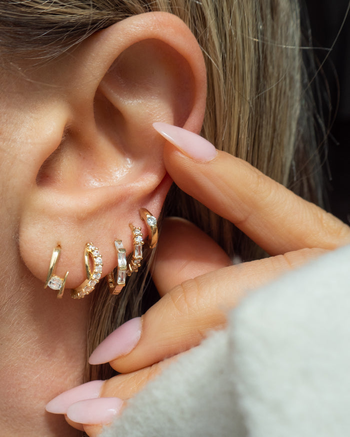 Close-up of an ear with multiple gold and crystal earrings