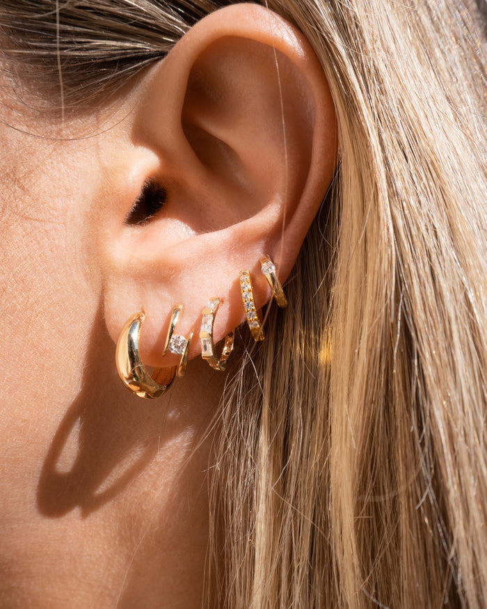 Close-up of an ear with multiple gold and crystal earrings