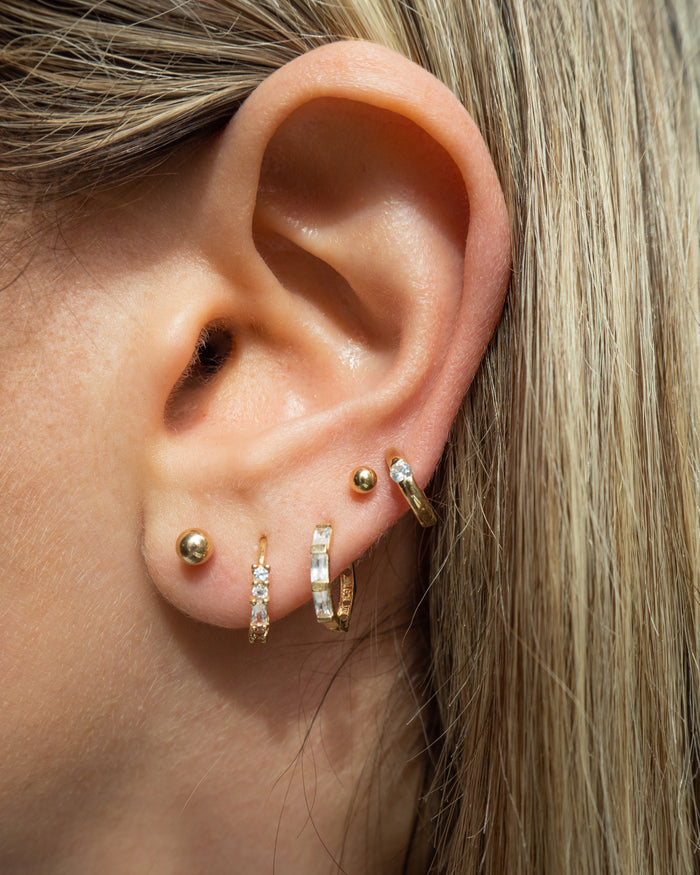 Close-up of an ear with multiple gold and crystal earrings