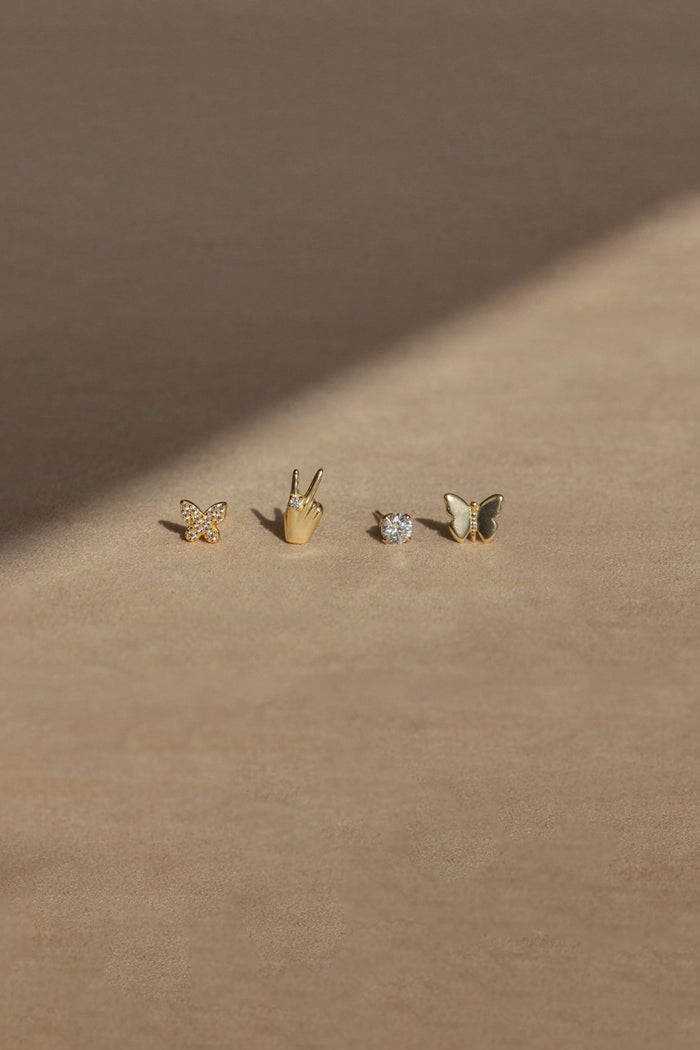 Four different gold stud earrings on a neutral background
