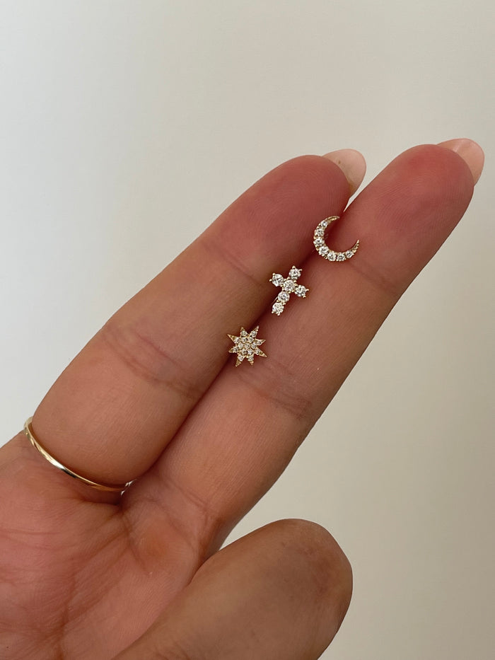 A hand holding three stone stud earrings