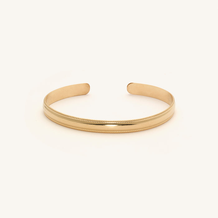Close up of a gold cuff bracelet on a white background