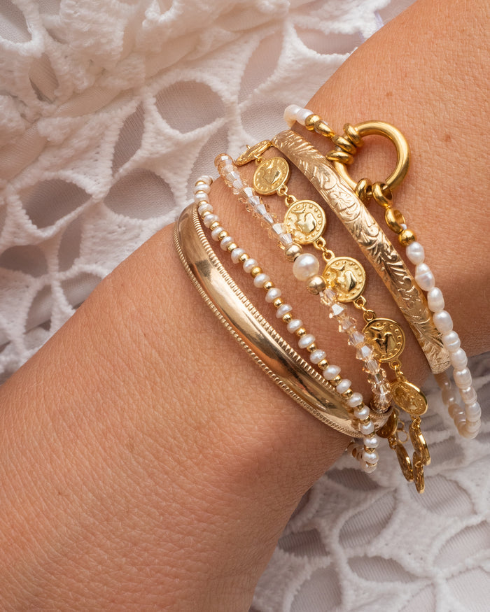 A wrist with gold and stone bracelets on a white fabric background