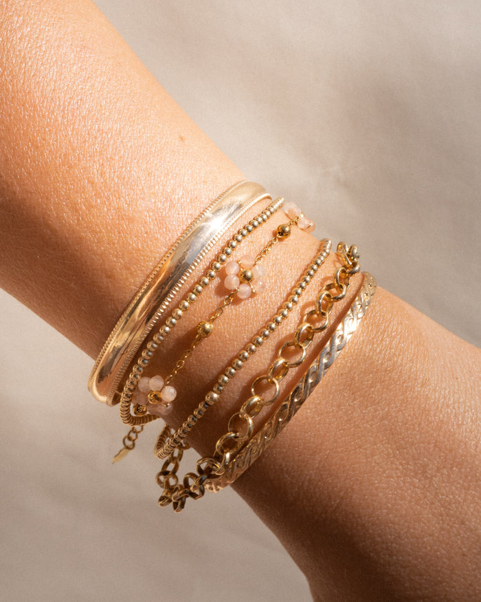 A wrist with gold and stone bracelets on a neutral background
