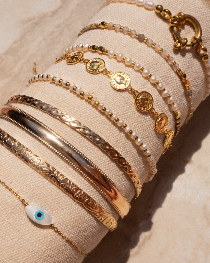A beige jewelry holder with assorted gold and stone bracelets on a tan stone background