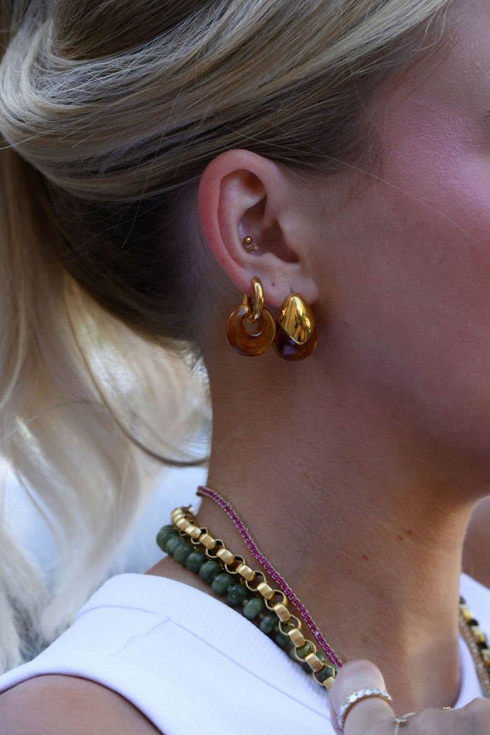 A woman wearing statement gold and stone earrings and necklaces