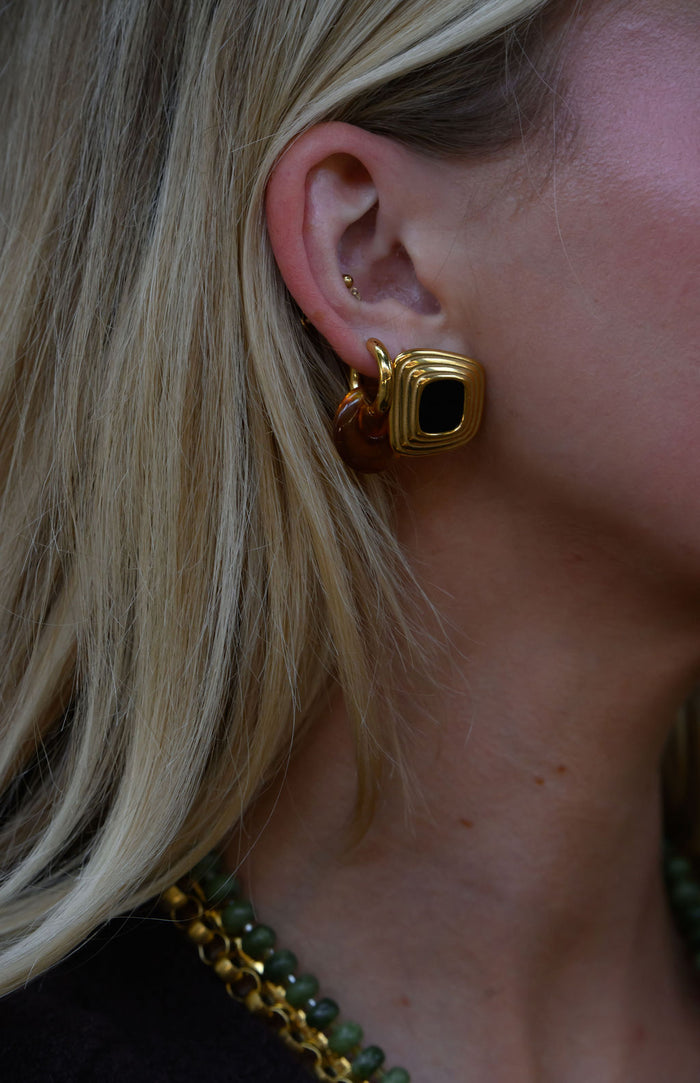 A woman wearing statement gold and stone earrings and necklaces