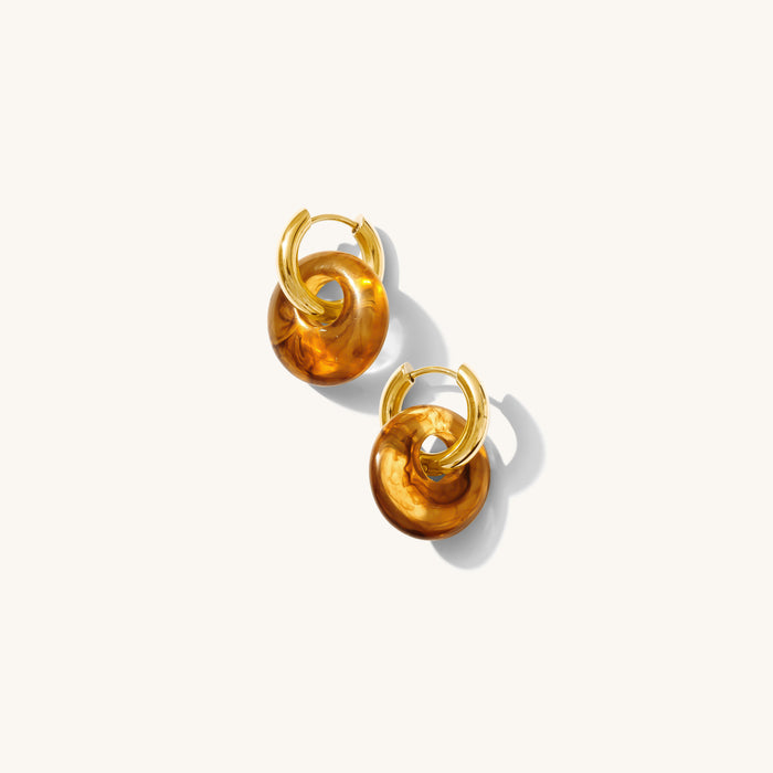 Close up of gold huggie earrings with removable resin charms on a white background