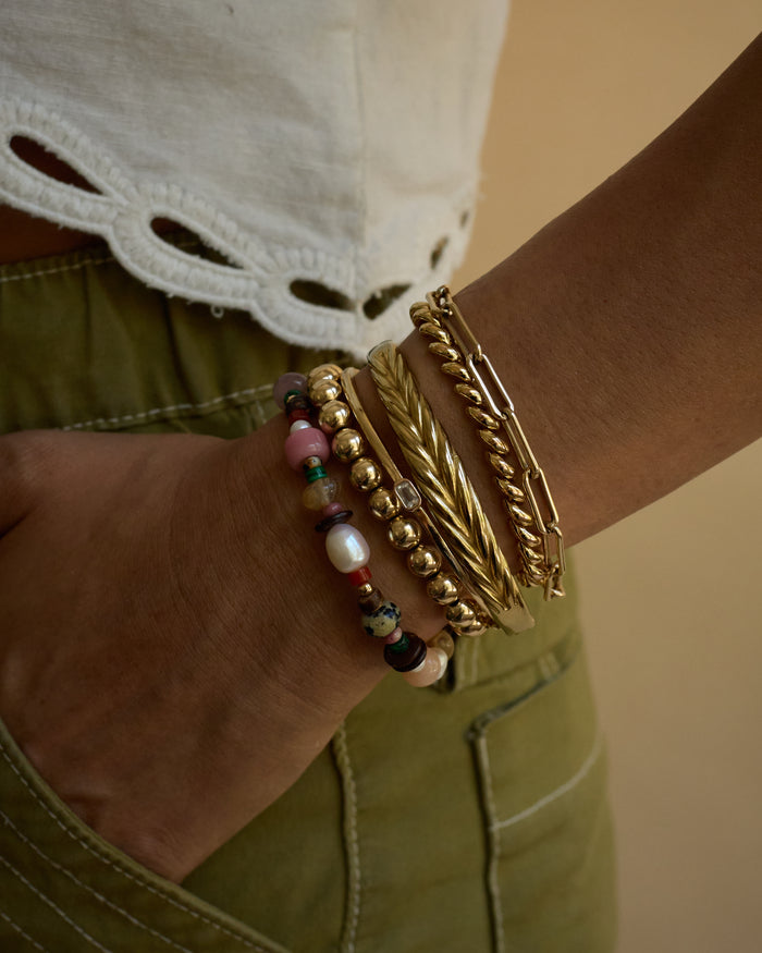 Close-up of a wrist wearing gold bracelets with colorful beads against a neutral background