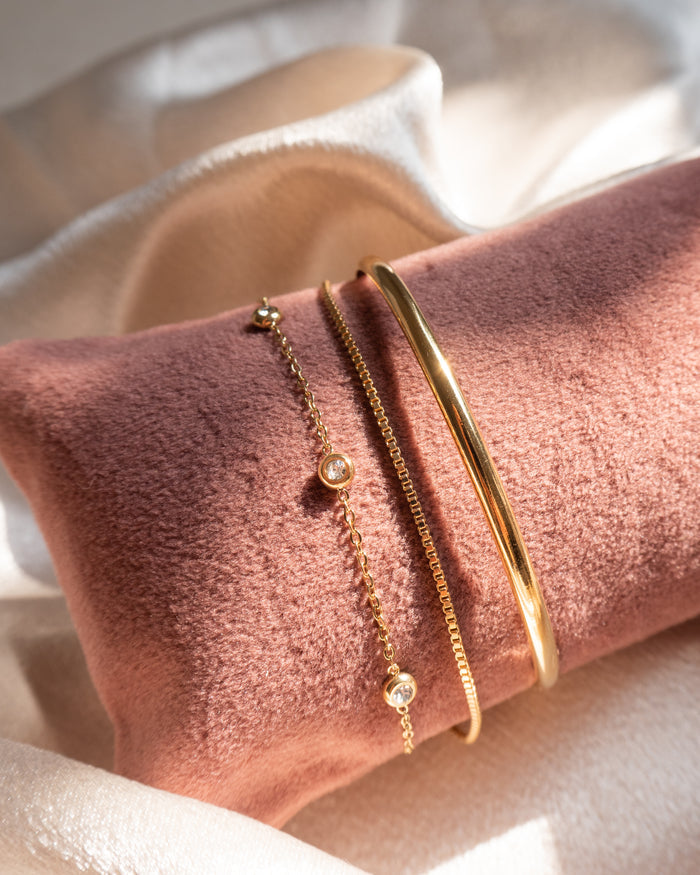 Close up of gold and stone bracelets on a pink jewelry pillow against a white background