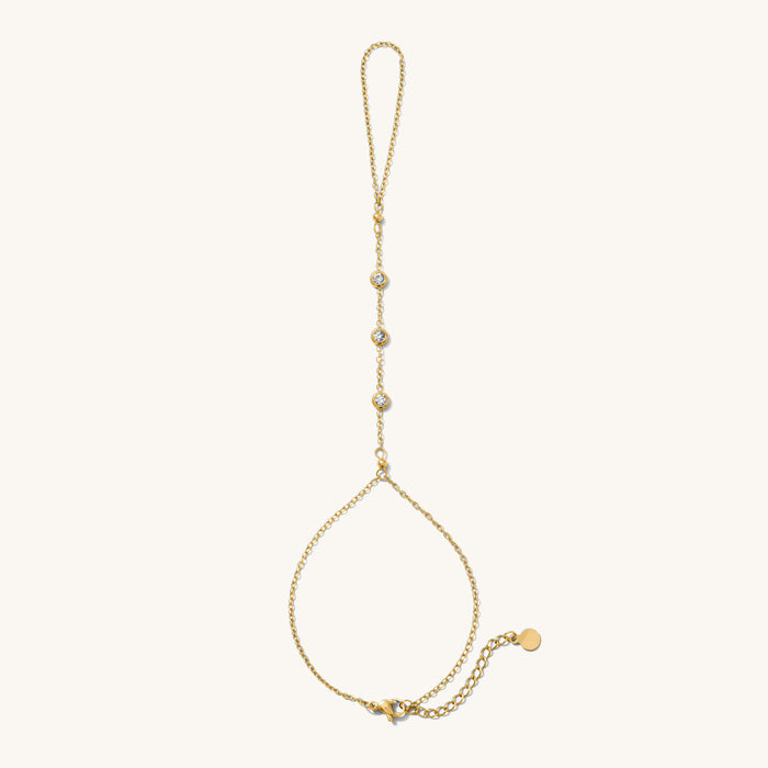 Close up of gold hand chain with stone accents on a white background
