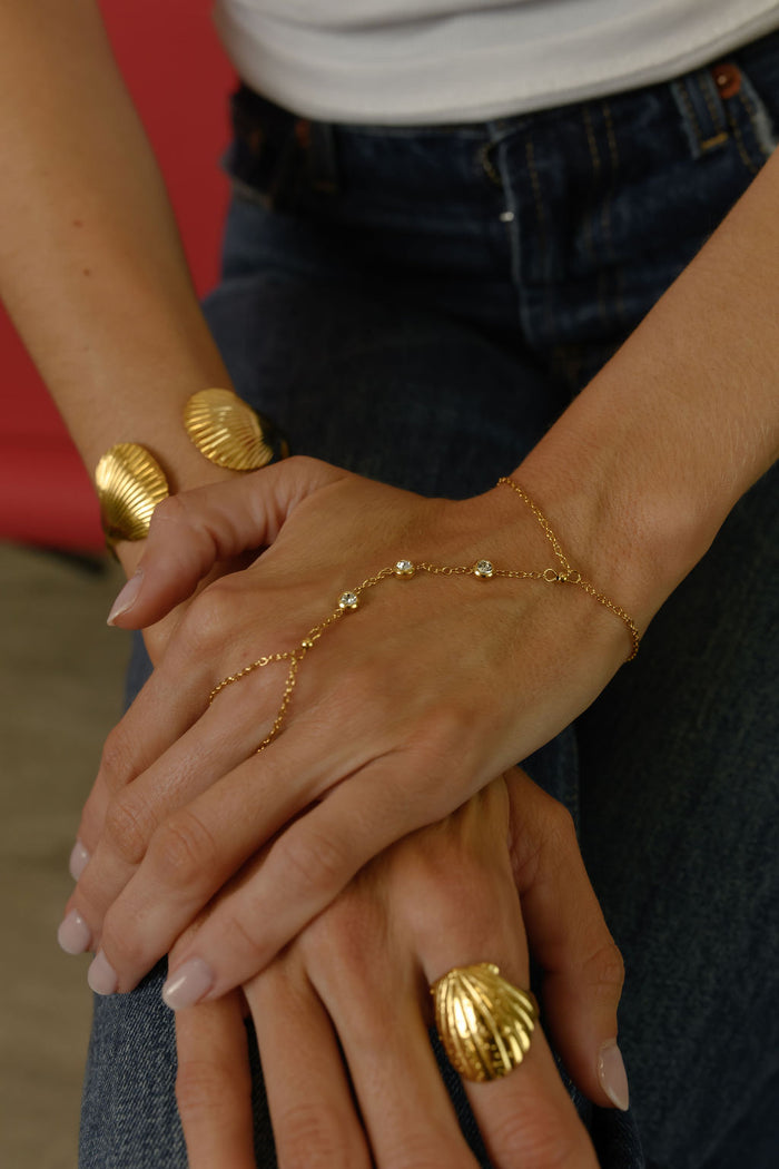 Close up of a person's hands with gold rings and bracelets resting on a pair of jeans