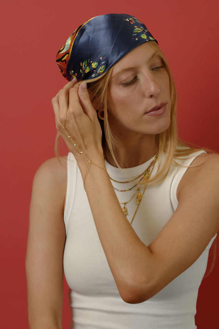 A woman in a blue bandana and white shirt wearing gold jewelry against a red background