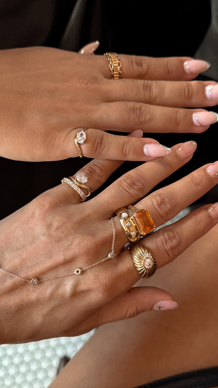 Close-up of hands wearing multiple gold and silver rings on a neutral background