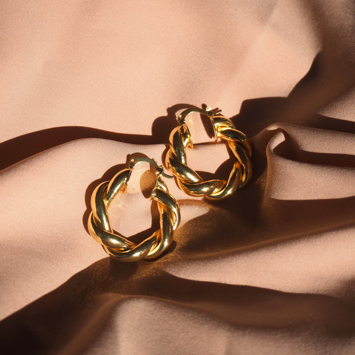 Close up of twisted gold hoops on a neutral cloth background