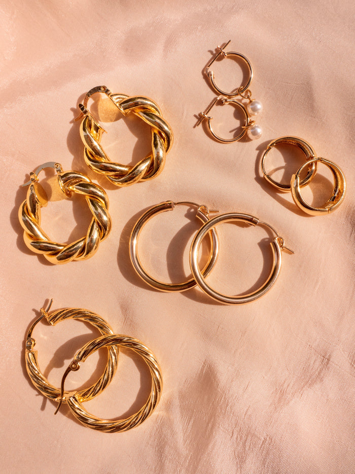 Five pairs of gold hoop earrings on a textured neutral background