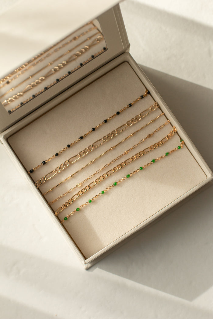 Dainty gold bracelets laid out in a beige jewelry box against a white background