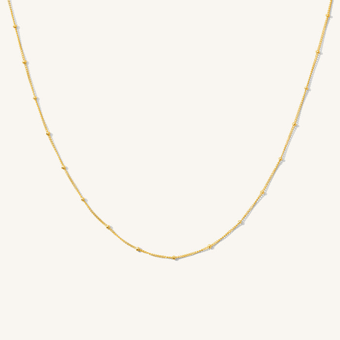 Close up of the gold Azin bead and cable chain necklace on a white background