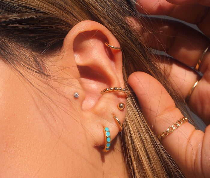 Close-up of an ear with multiple dainty gold earrings