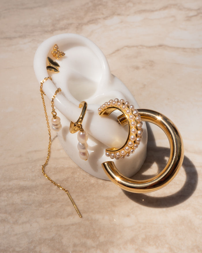 An ear model prop with various gold and pearl earrings