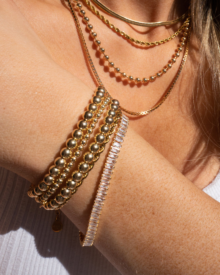 A person wearing a white shirt and assorted gold and stone bracelets and necklaces