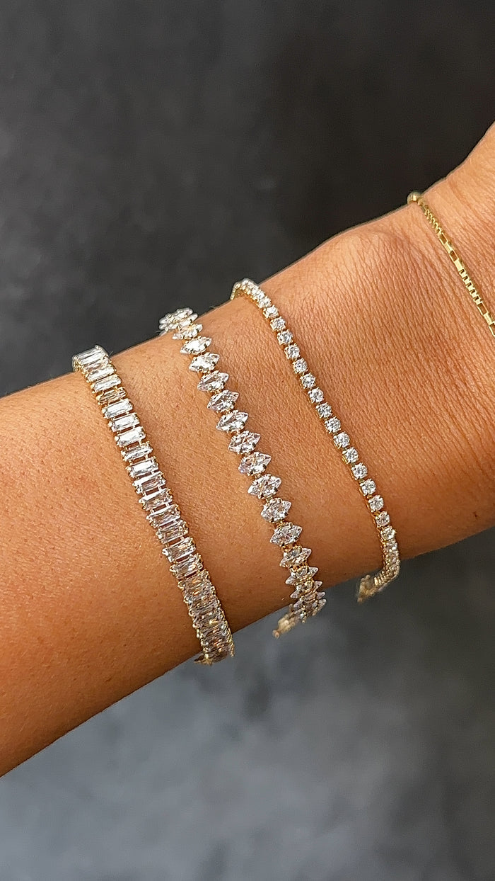 Close up of a wrist with different tennis bracelets on a grey background