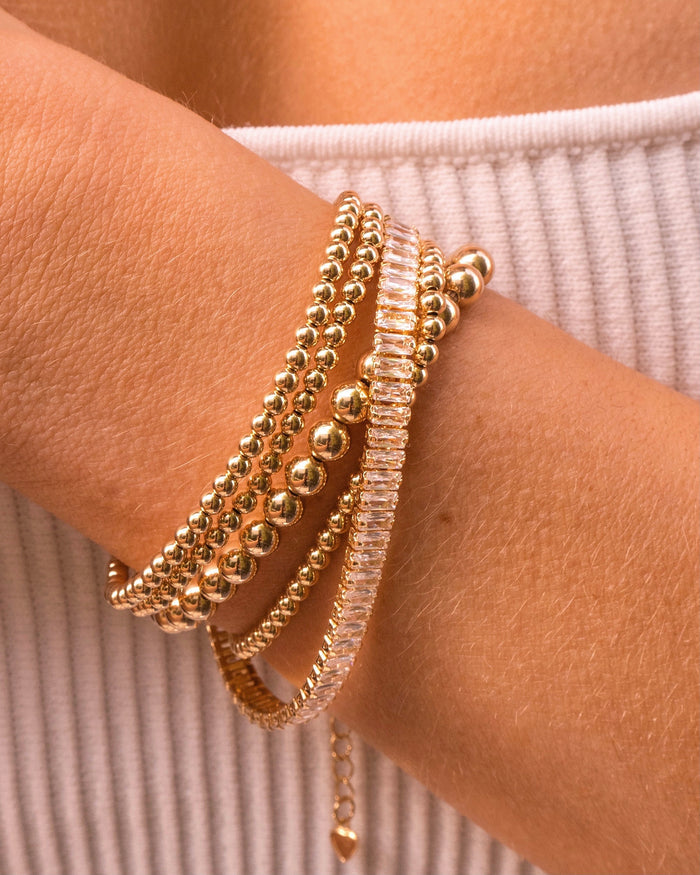 Close up of a person's wrist with gold and stone bracelets against their white tank top
