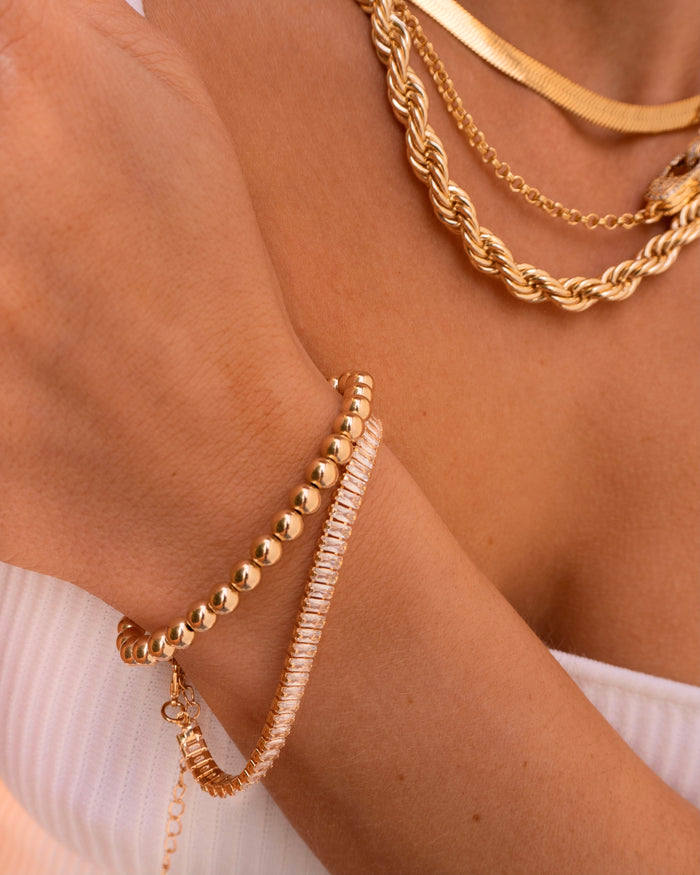 Close up of a person wearing a white tube top, gold necklaces, and gold bracelets