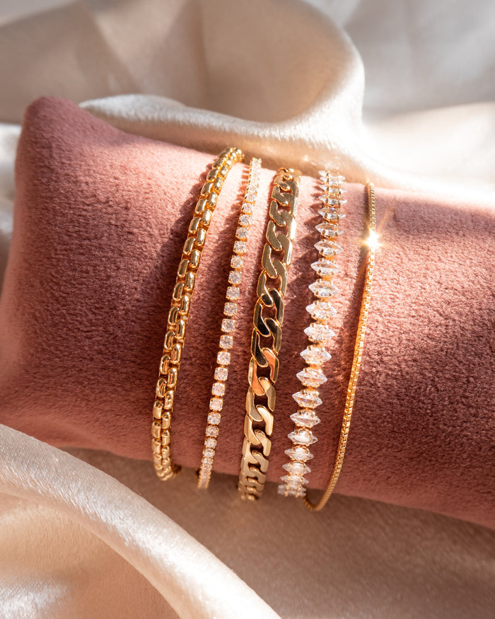Close up of gold and stone bracelets on a pink jewelry pillow against a white background