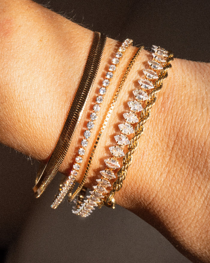 Close up of a wrist with gold and stone bracelets on a brown background