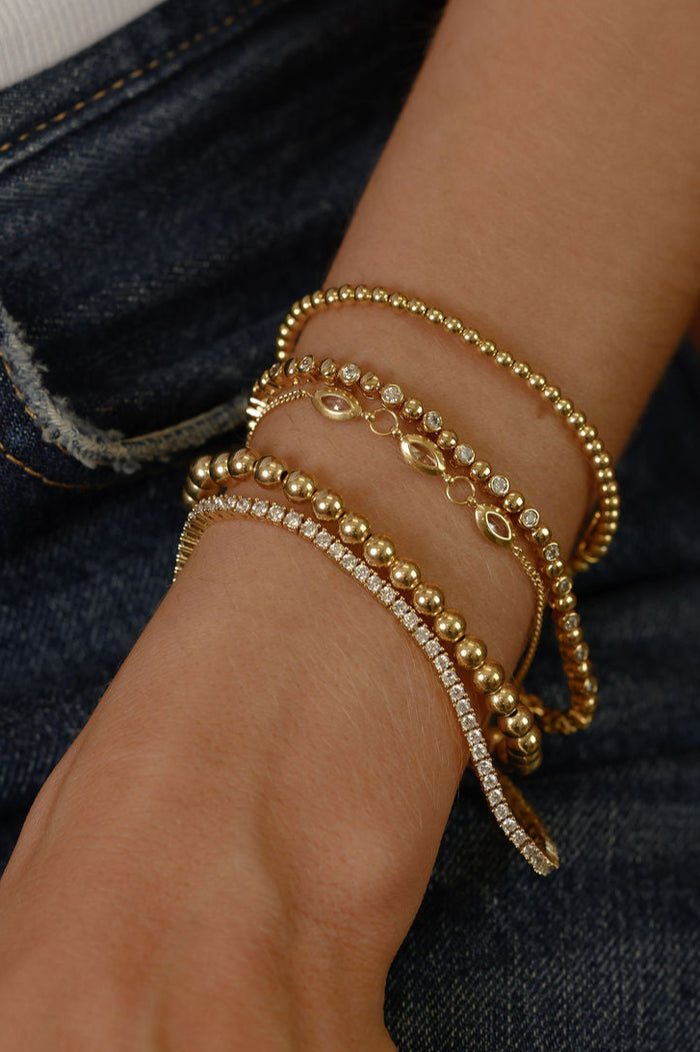 Close up of a wrist with gold and stone bracelets on a pair of jeans