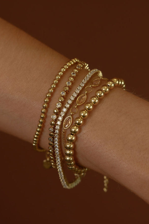 Close up of a wrist with assorted gold and stone bracelets on a brown background