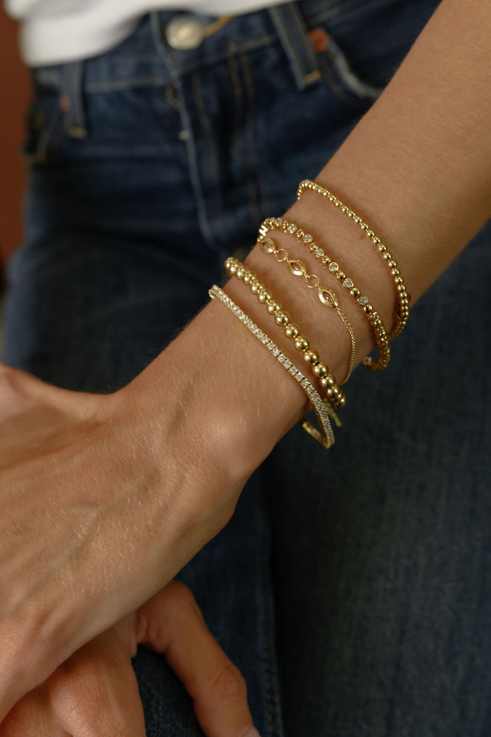 Close up of a person wearing gold bracelets and blue jeans against a brown background