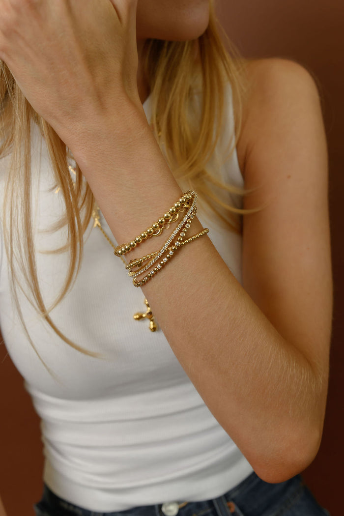 Close up of a person wearing gold bracelets and a white tank top against a brown background
