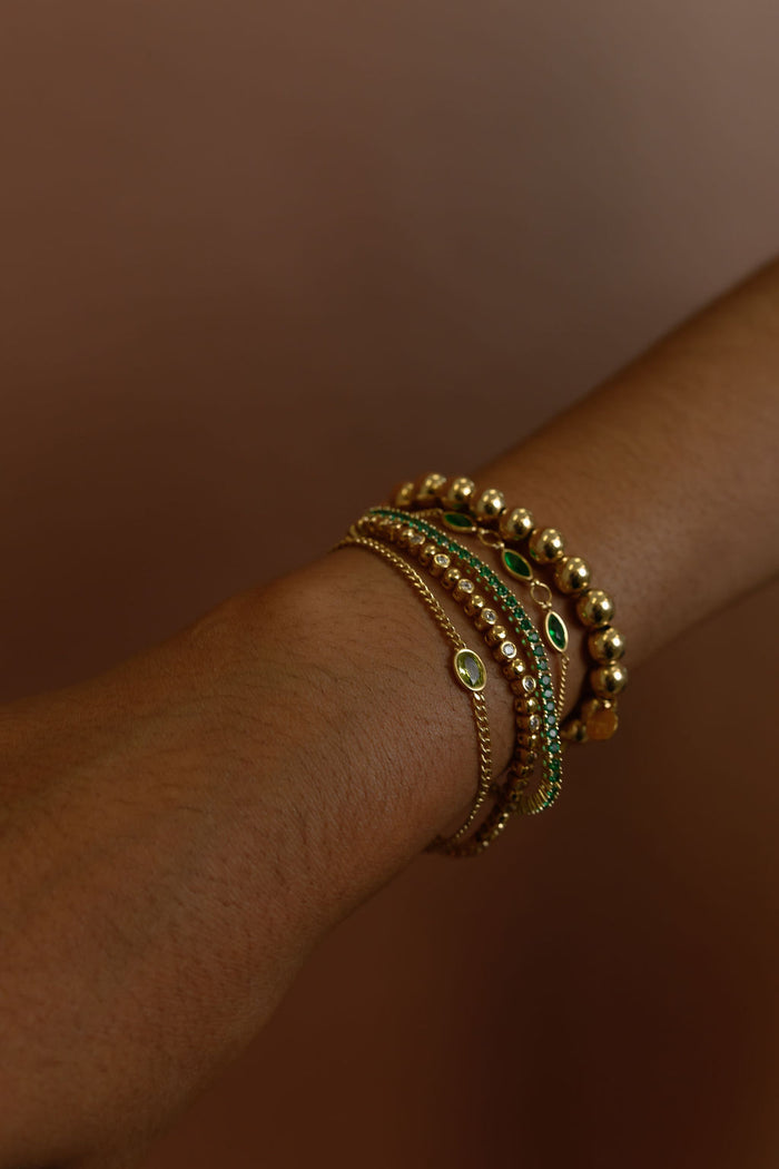 Close up of a wrist with gold and stone bracelets on a brown background