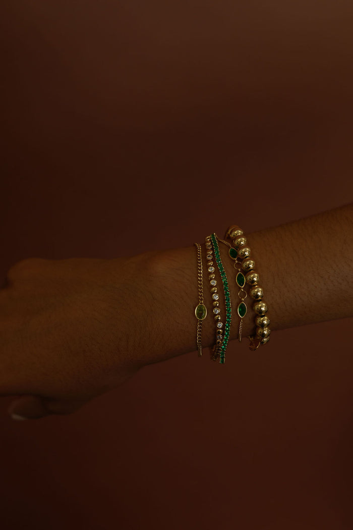 Close up of a wrist with gold and stone bracelets on a brown background