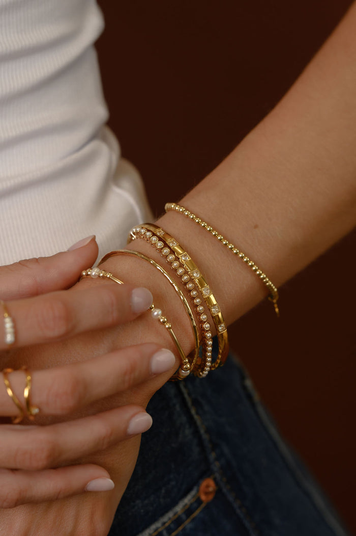 Close up of a wrist with gold bracelets on a brown background