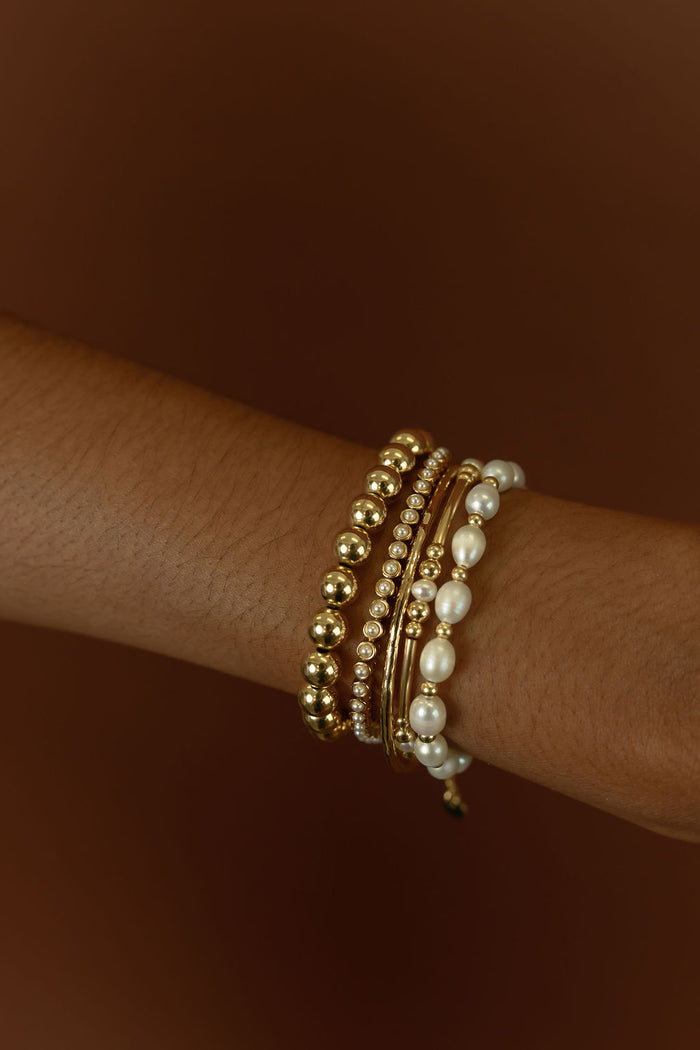 Close up of a wrist with gold bracelets on a brown background