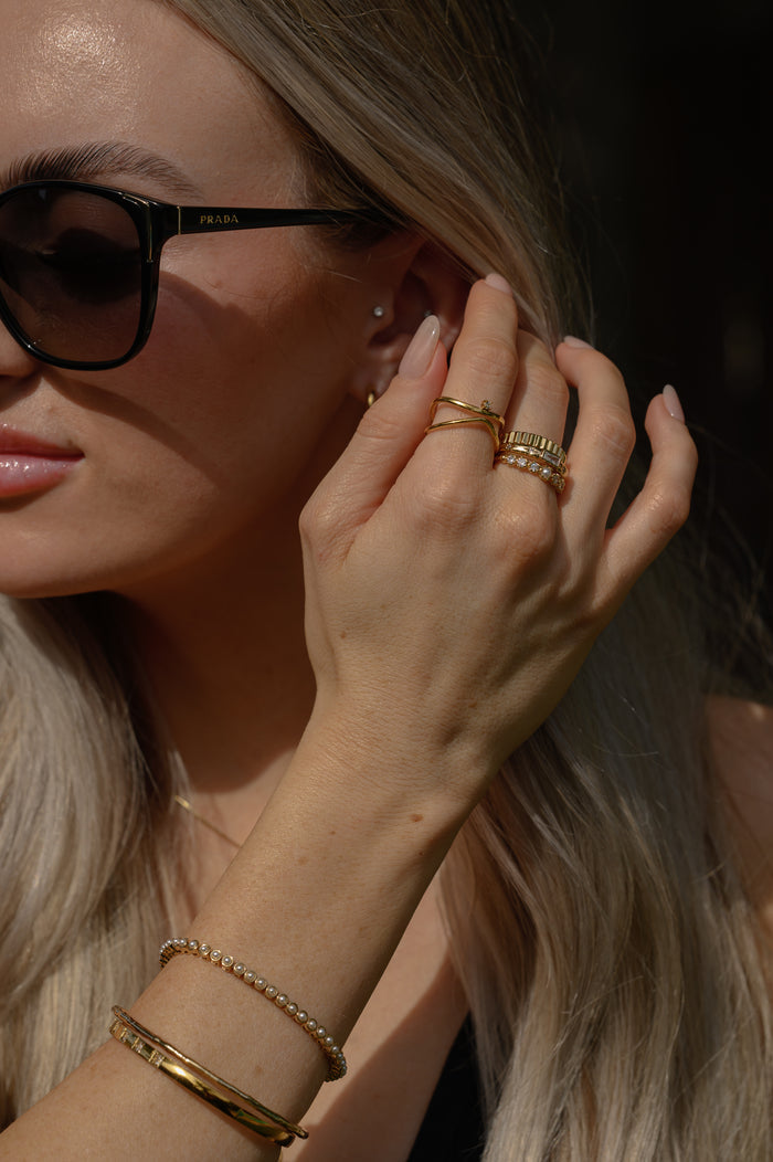 A woman wearing sunglasses, gold rings, and gold bracelets