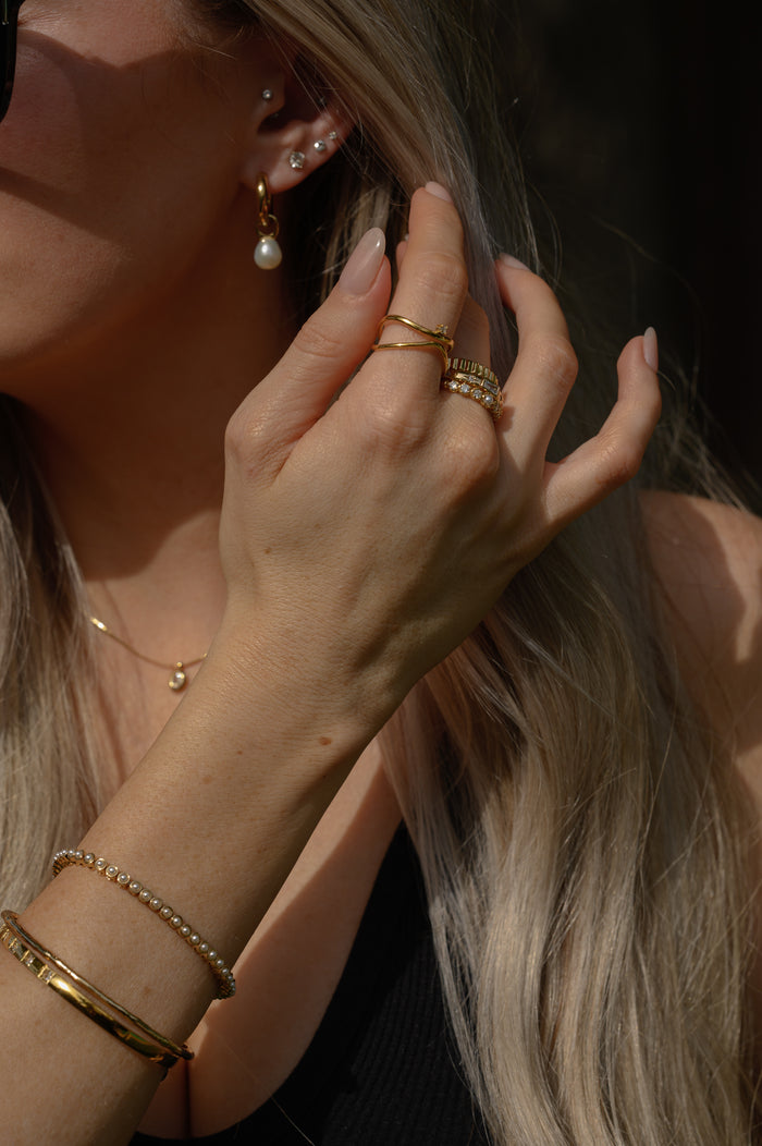 A woman wearing a black tank top, gold rings, and gold bracelets