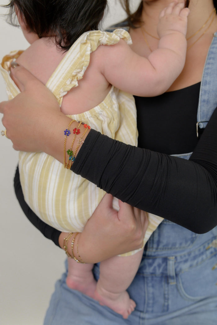 Close up a person wearing a black shirt, blue overalls, and various stone bracelets and rings carrying a child