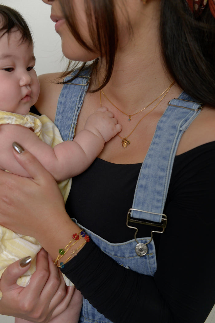 Close up a person wearing a black shirt, blue overalls, and various stone bracelets and necklaces carrying a child