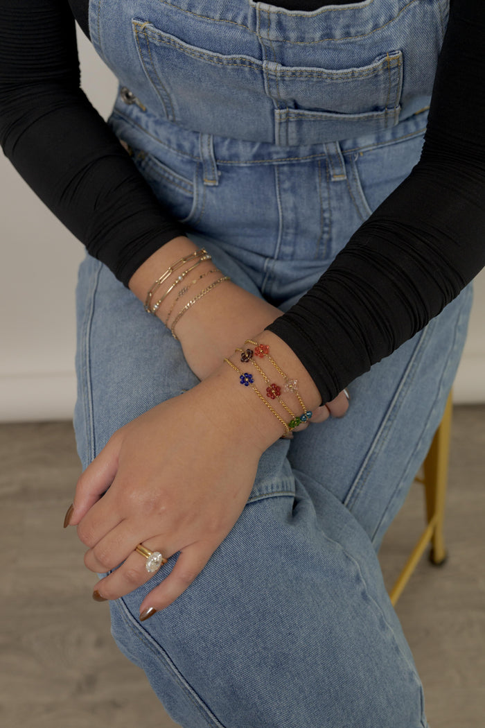 Close up a person wearing a black shirt, blue overalls, and various stone bracelets